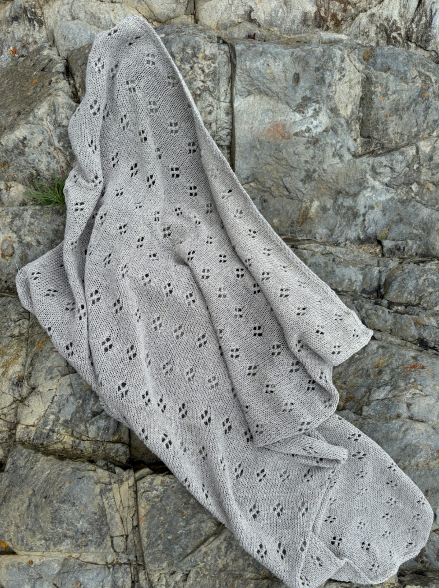 image shows a grey hand knitted organic swaddle baby blanket