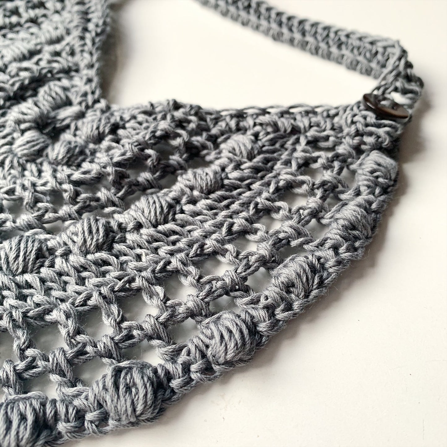 image shows the crochet detail of a grey organic cotton baby bib