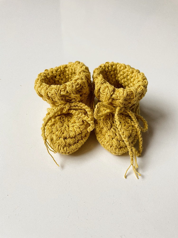 Image shows a pair of saffron yellow organic cotton baby booties.
