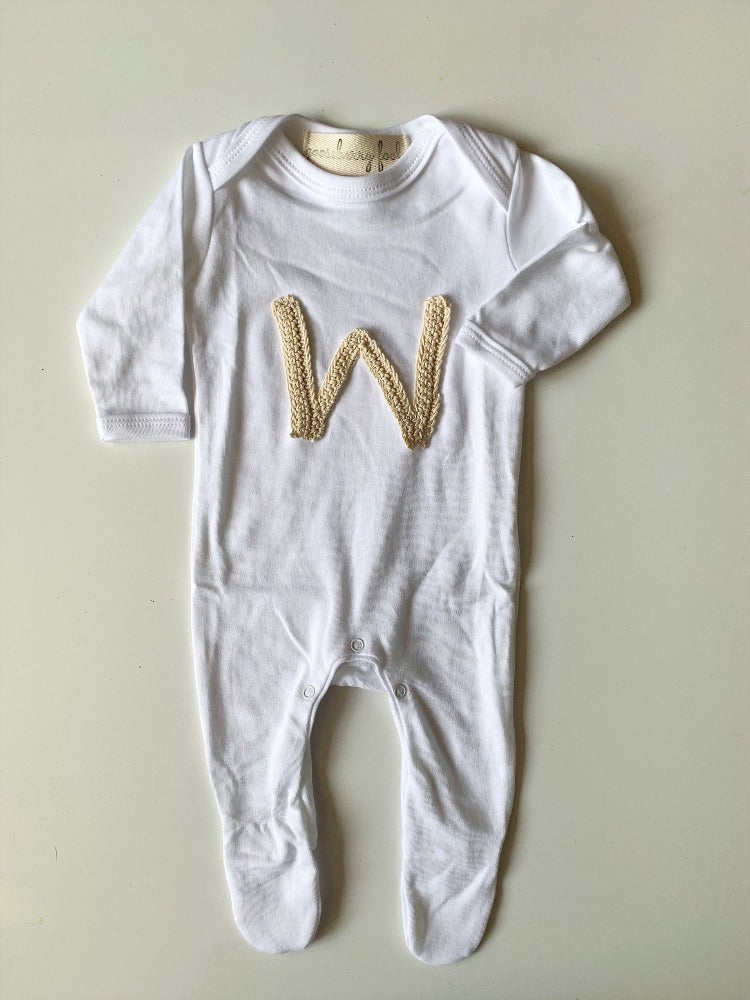Image shows an organic cotton romper personalised with a neutral coloured crochet initial on.