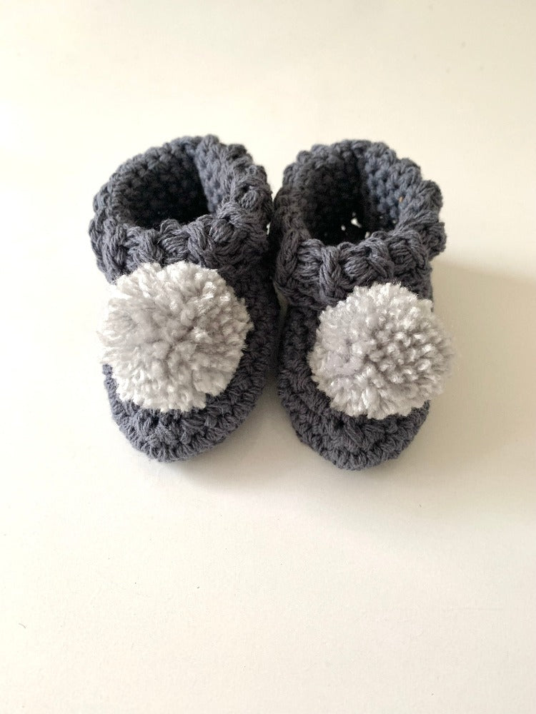 Image shows a pair of blue organic cotton baby booties with grey pom pom