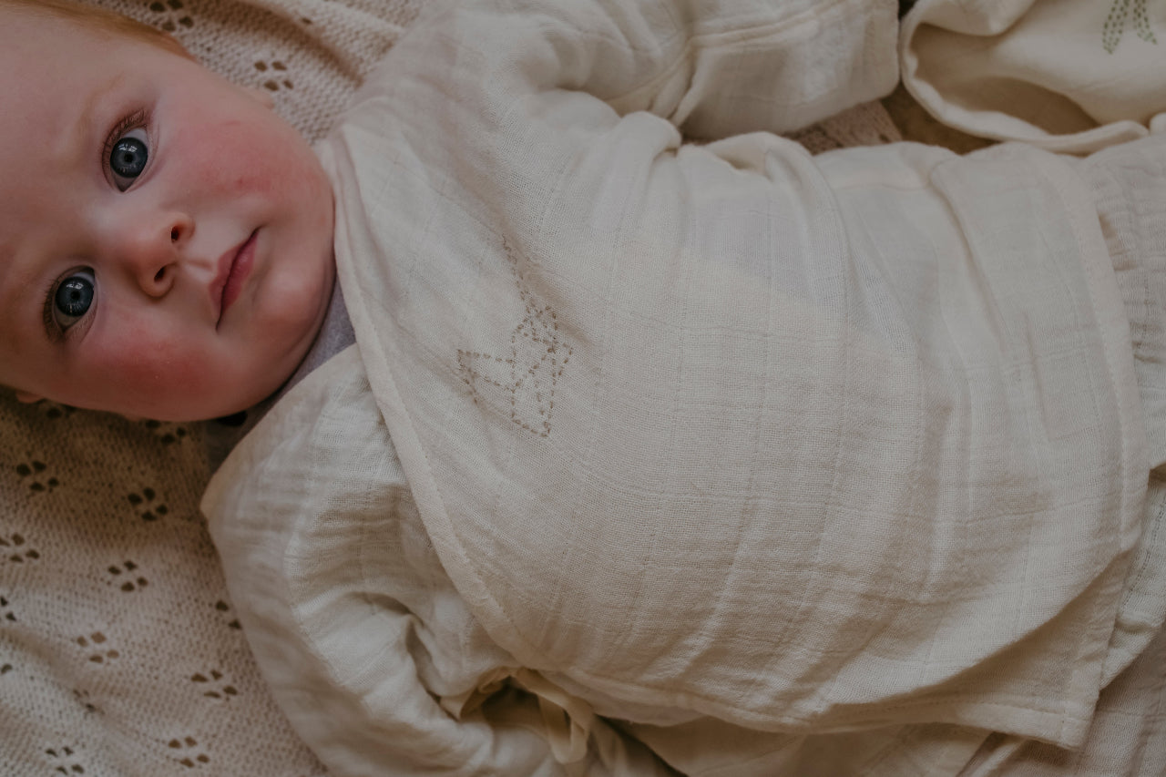Baby wearing organic cotton muslin pyjamas on a textured surface