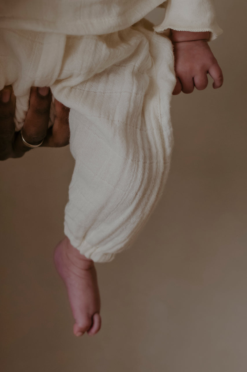 Close-up of a baby's feet wearing cream organic cotton pyjamas against a neutral background