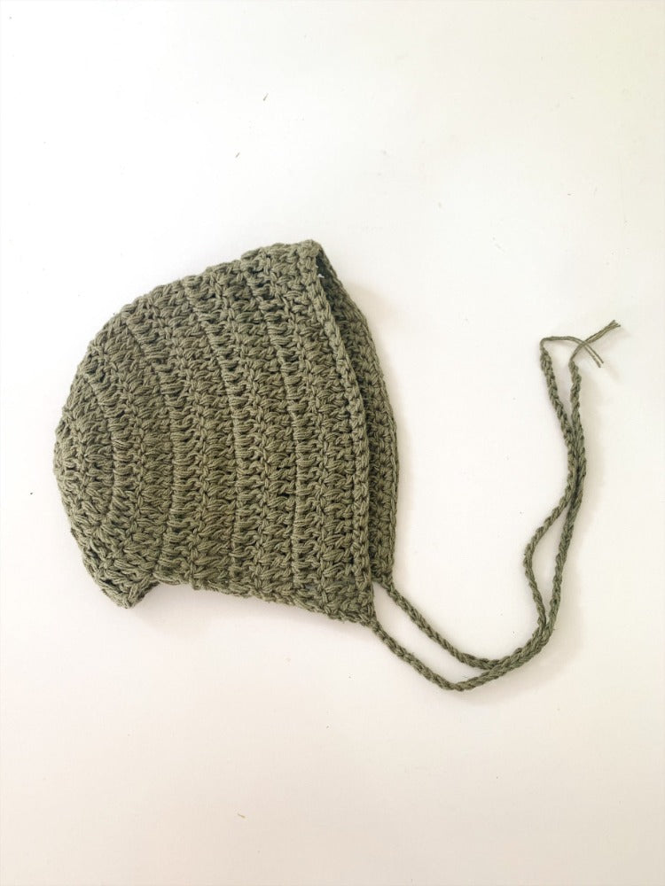 image shows a green coloured baby bonnet crocheted from organic cotton